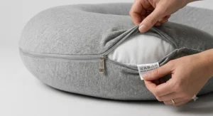 A woman using a C-shaped pregnancy pillow for upright back support while relaxing in bed.