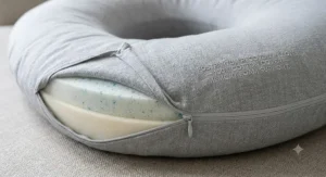 A close-up view showing the removable, washable fabric cover being held by a hand next to the postpartum recovery pillow.