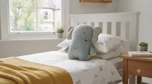 A smiling toddler hugs a patterned kids character pillow while sitting on a playful rug.