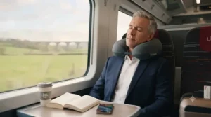 Traveller using an ergonomic neck pillow for comfort during a cross-country train journey.