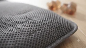 An extreme macro close-up photograph of the surface of the charcoal grey massage cushion, highlighting its durable, breathable, three-dimensional mesh fabric structure. The precise weave and texture are clearly visible.